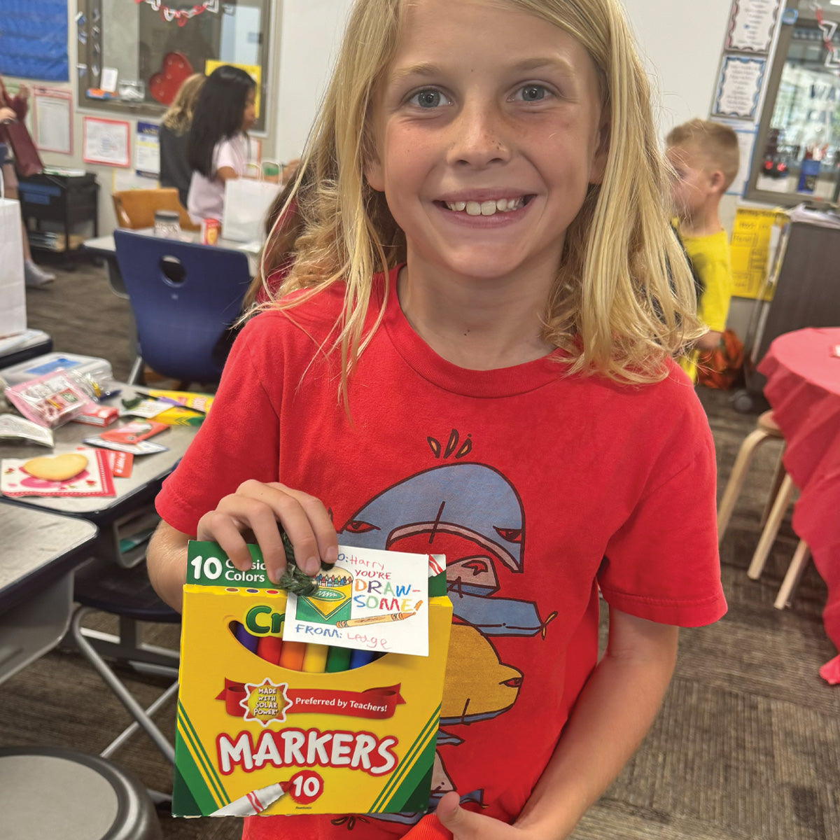 Child holding markers with You’re Draw-some printable Valentine tag for a classroom Valentine